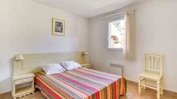 A bedroom with a bed, bedside table, chair, window, and a picture on the wall.