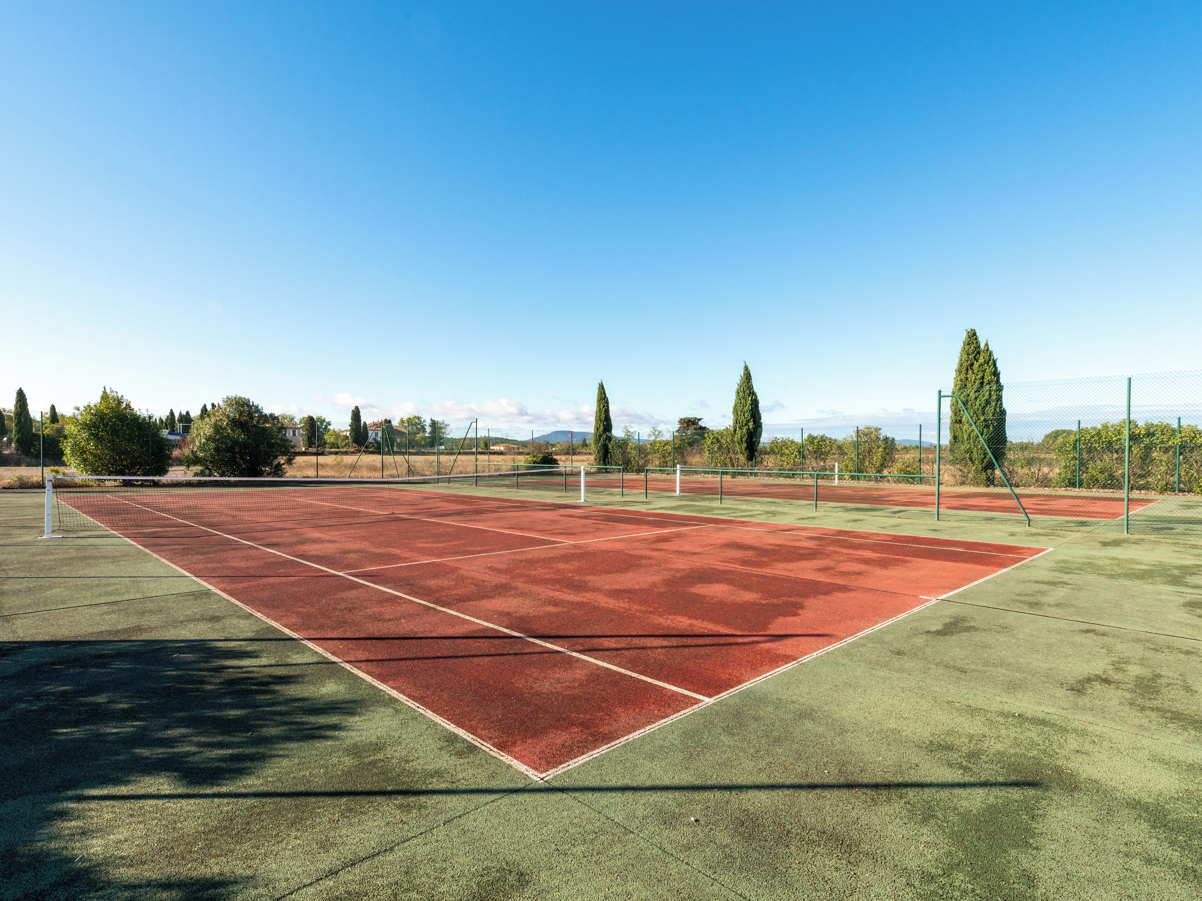 Un court de tennis avec un filet, entouré d’arbres et sous un ciel dégagé.
