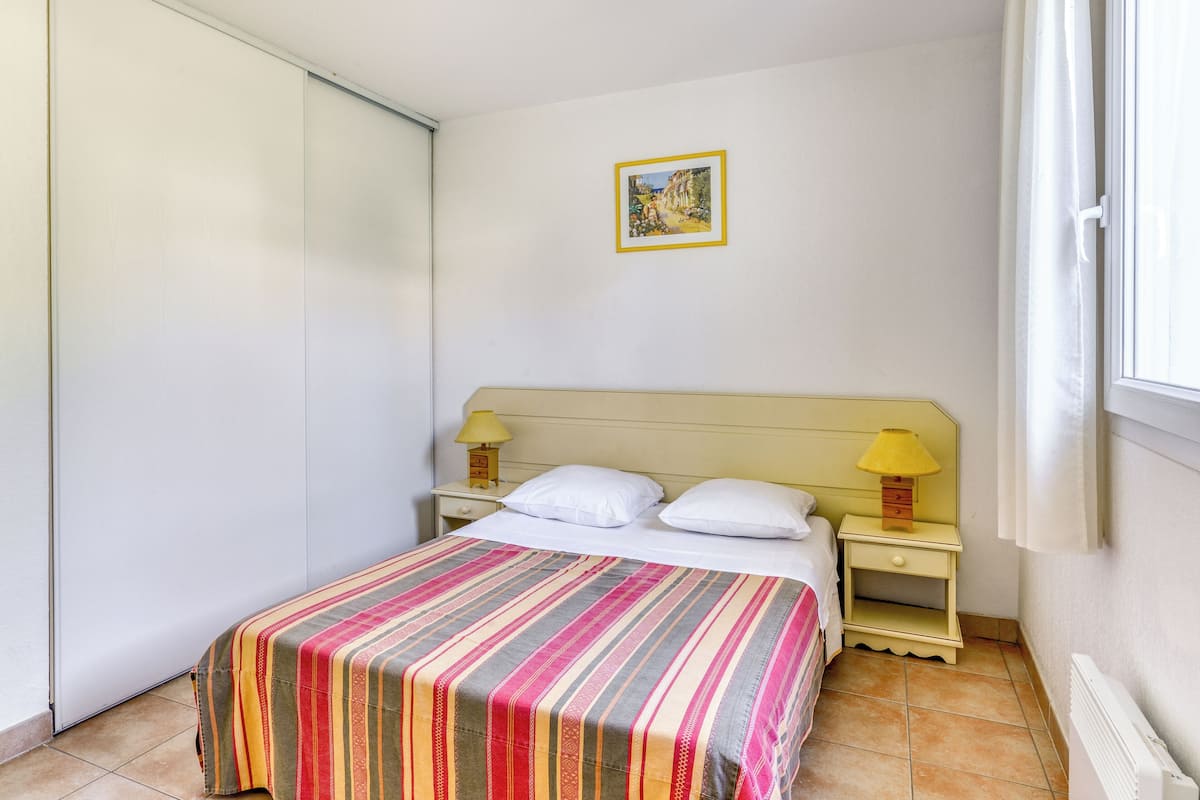 Une chambre à coucher avec un lit, deux tables de chevet avec des lampes, un tableau au mur et une fenêtre avec des rideaux.