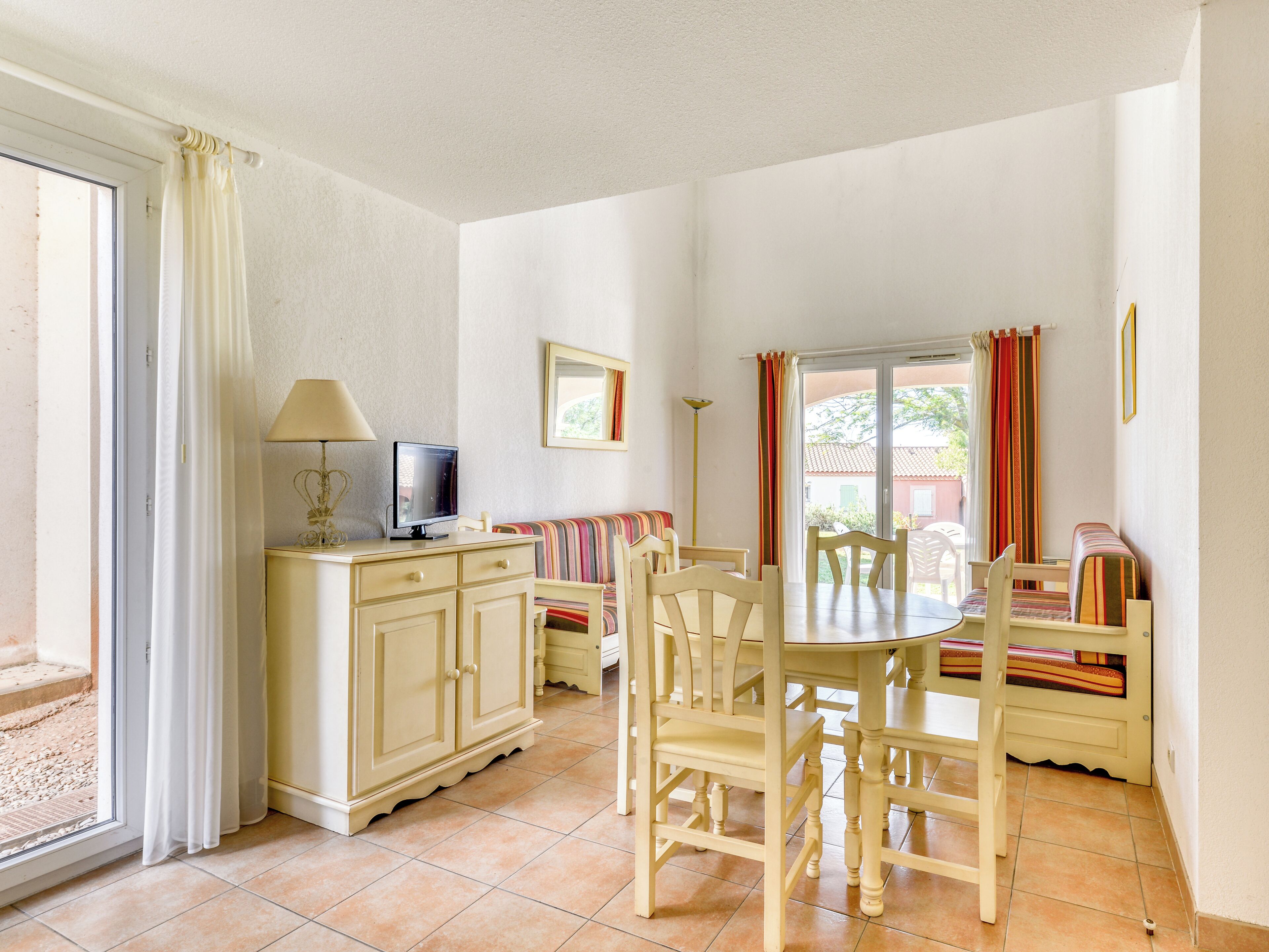 Un comedor con una mesa y sillas, un televisor sobre un mueble bajo y una ventana con cortinas.