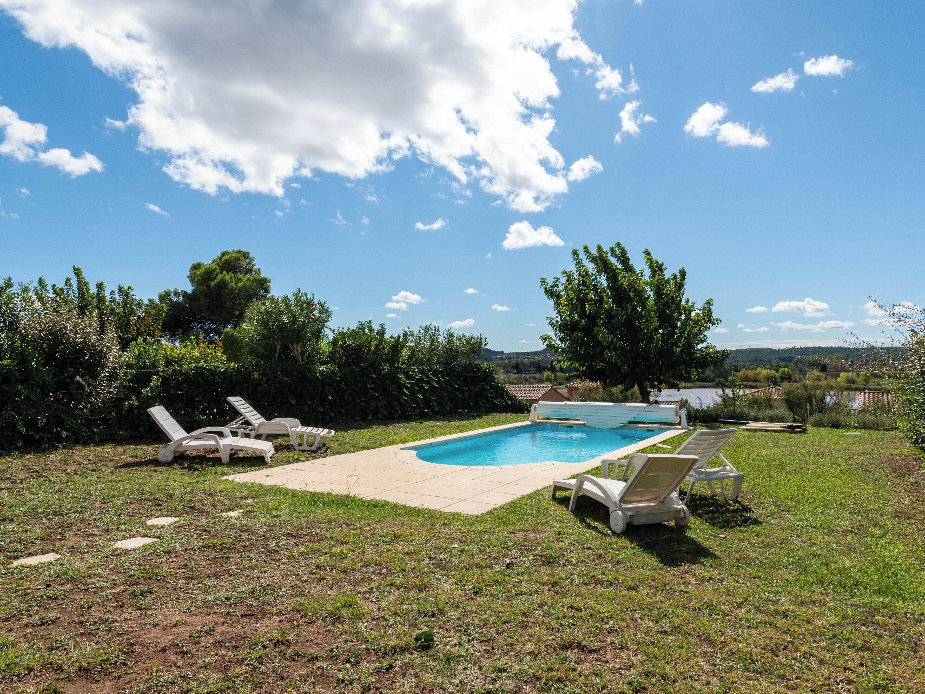 A swimming pool with lounge chairs, surrounded by a grassy area and trees.
