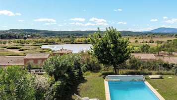 Una piscina con borde de baldosas, rodeada de follaje y vistas a un lago y colinas distantes.