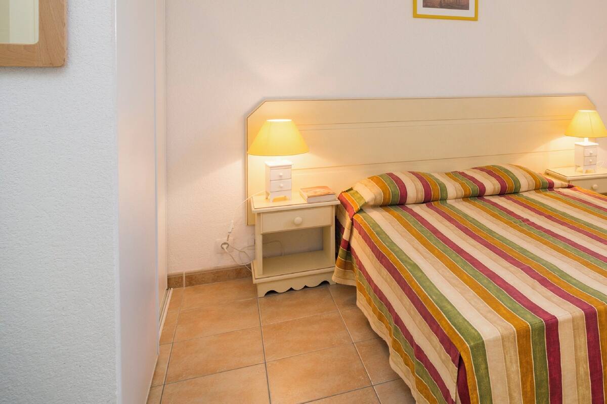 Une chambre à coucher avec un lit, deux lampes de chevet, une table de nuit, un tableau encadré au mur et un sol carrel é.