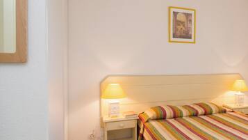 A bedroom with a bed, two bedside lamps, a nightstand, a framed picture on the wall, and a tiled floor.
