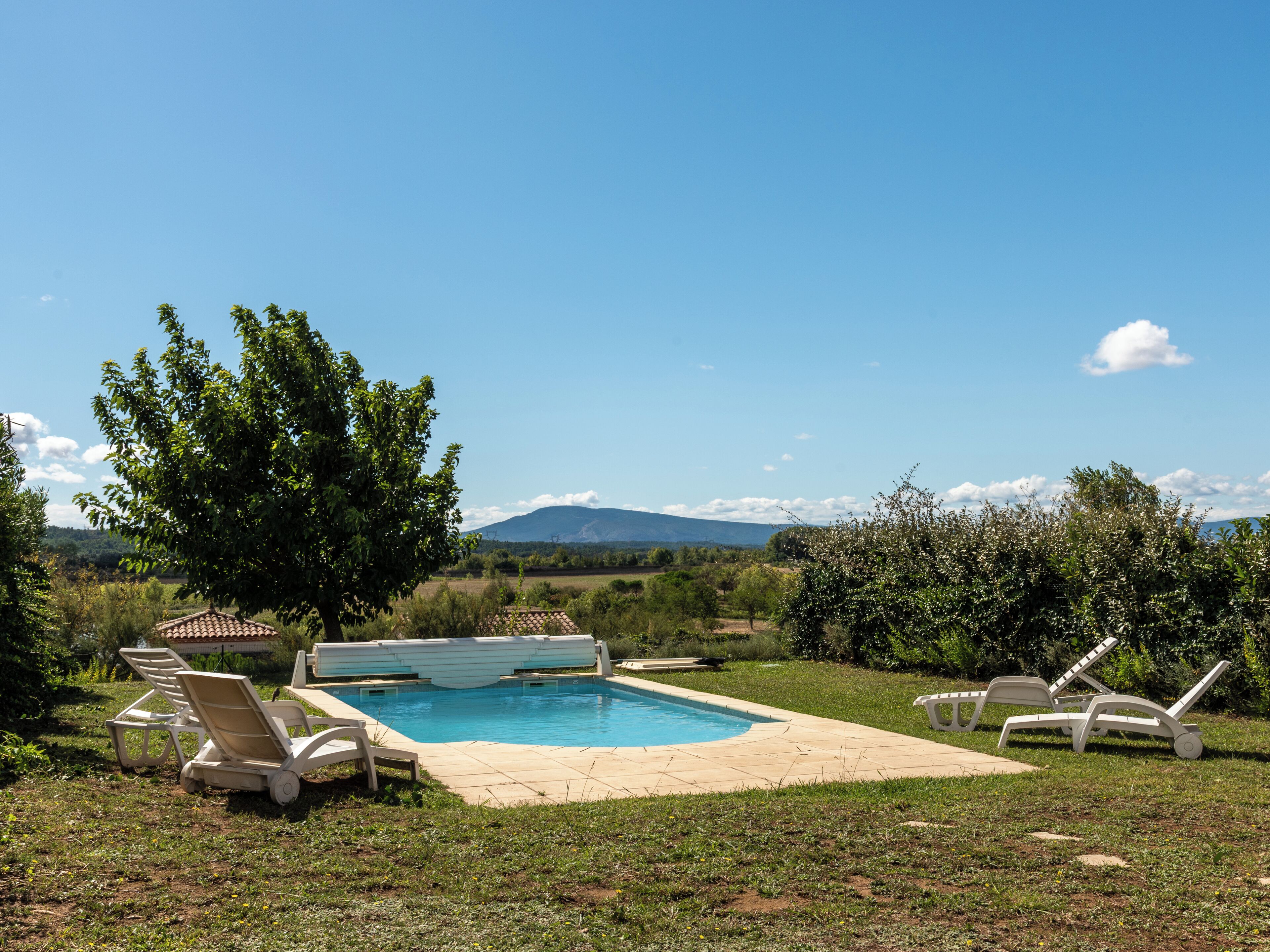 Una piscina con sillones de descanso, rodeada de follaje y montañas al fondo.