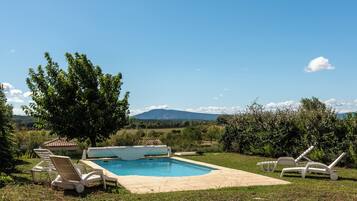 Una piscina con sillones de descanso, rodeada de follaje y montañas al fondo.