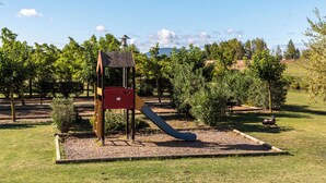 A playground with a slide and climbing structures, surrounded by grass and trees. - Vacancéole - Port Minervois (Homps)