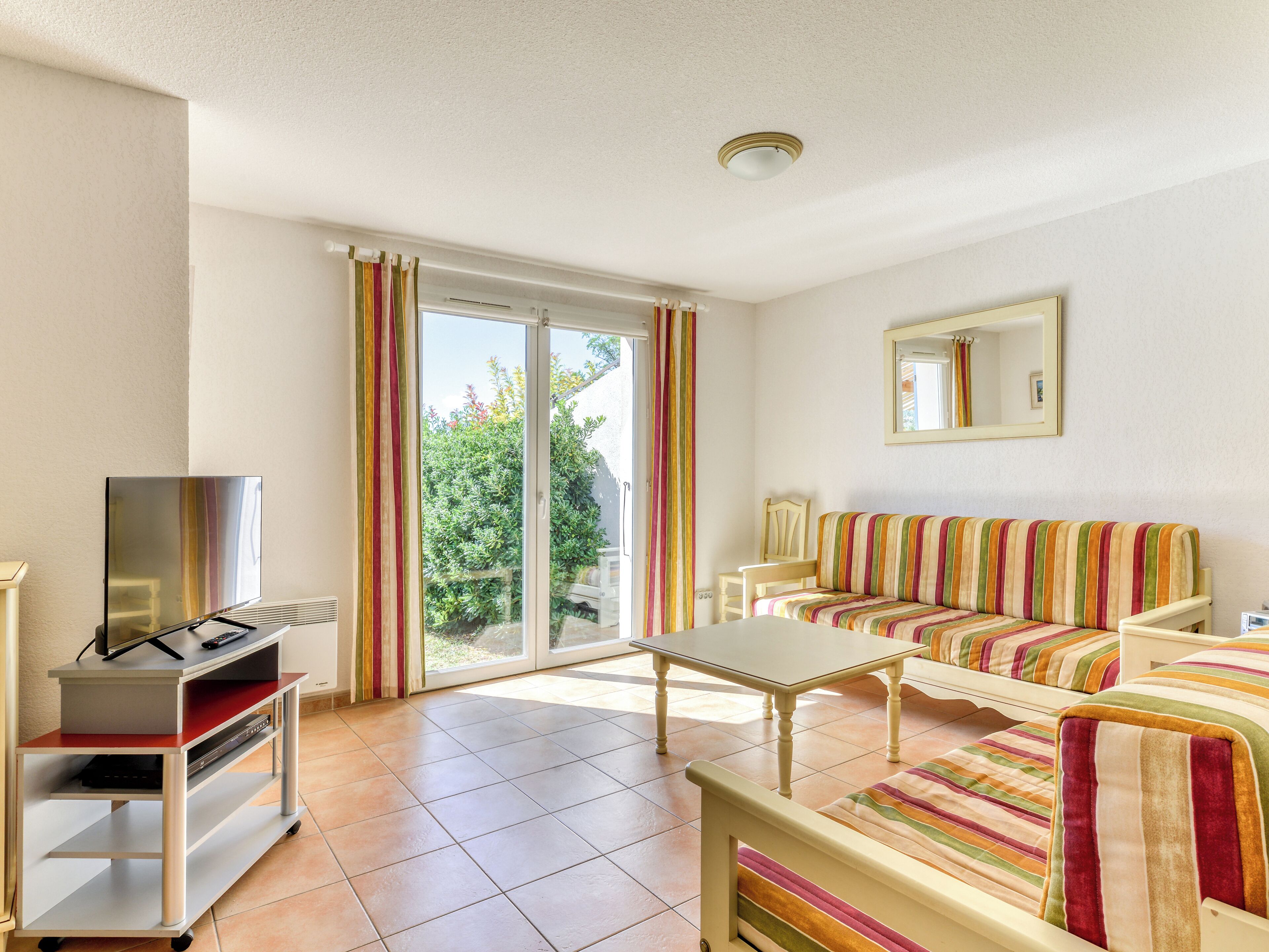 Amplia sala de estar con un sofá, un televisor sobre un mueble, una mesa y un puerta corrediza de vidrio que da a un balcón.