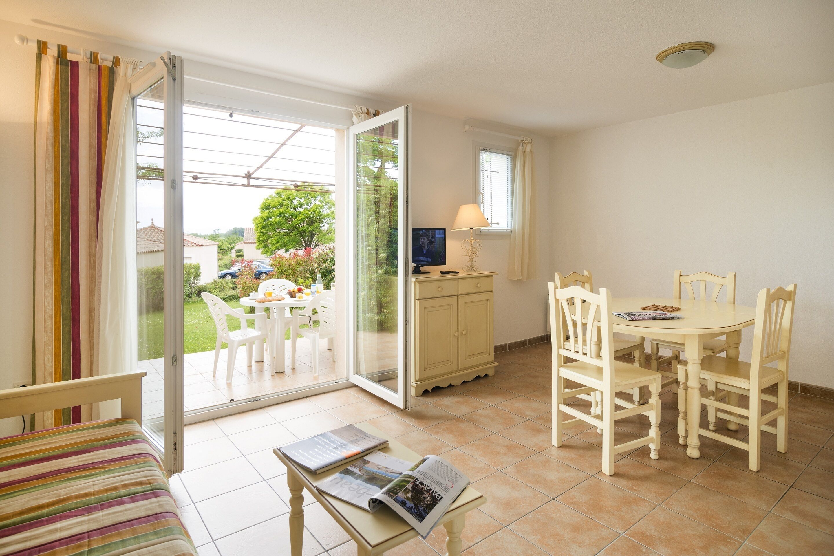 A room with a bed, a table with chairs, a television, and a sliding glass door leading to an outdoor area with a table and chairs.
