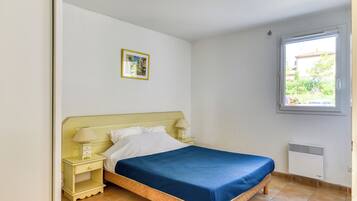 Een slaapkamer met een bed, nachtkastjes, een raam en een schilderij aan de muur.