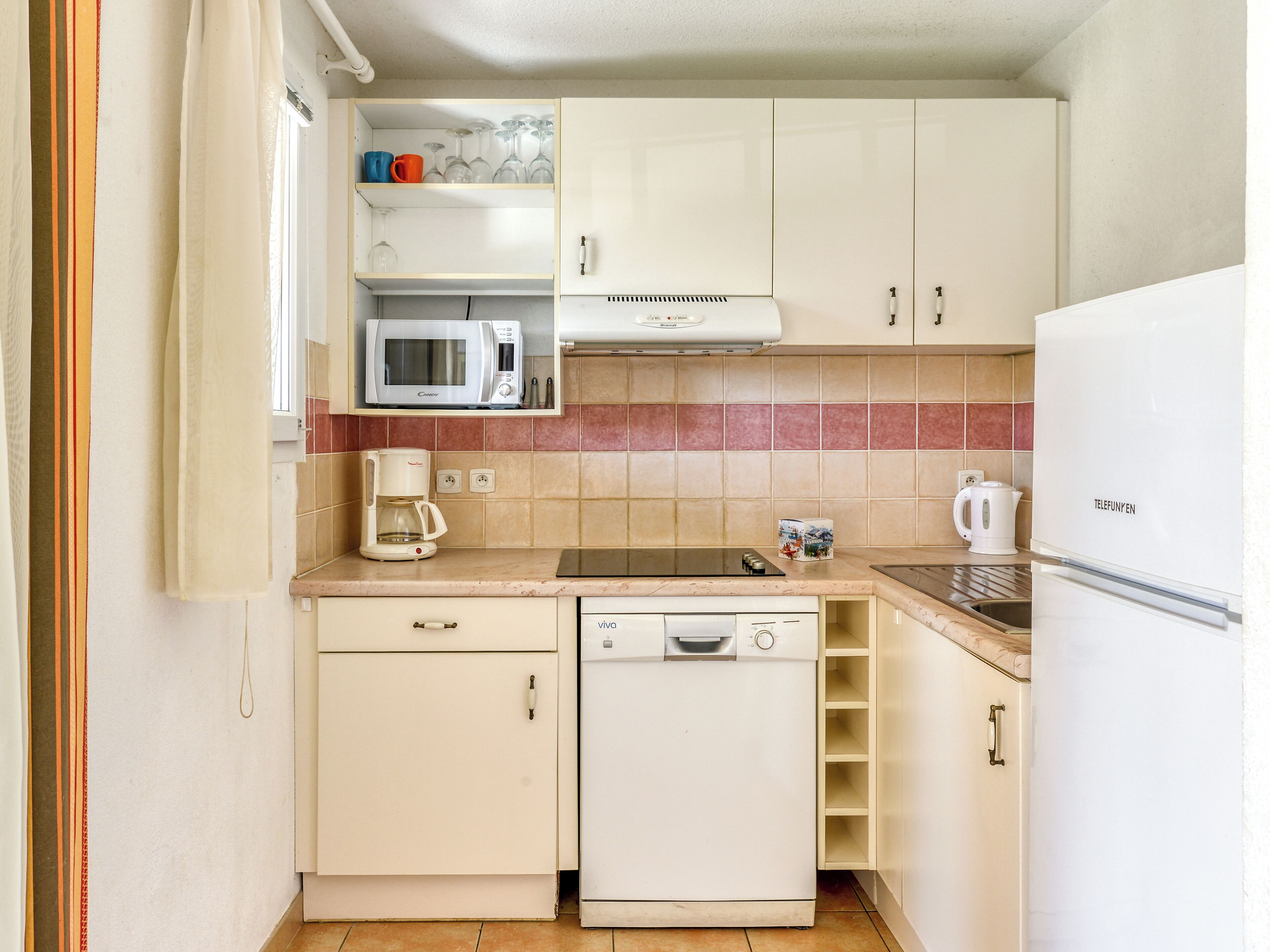 Eine kompakte Küche mit Mikrowelle, Kaffeemaschine, Geschirrspüler und Kühlschrank.
