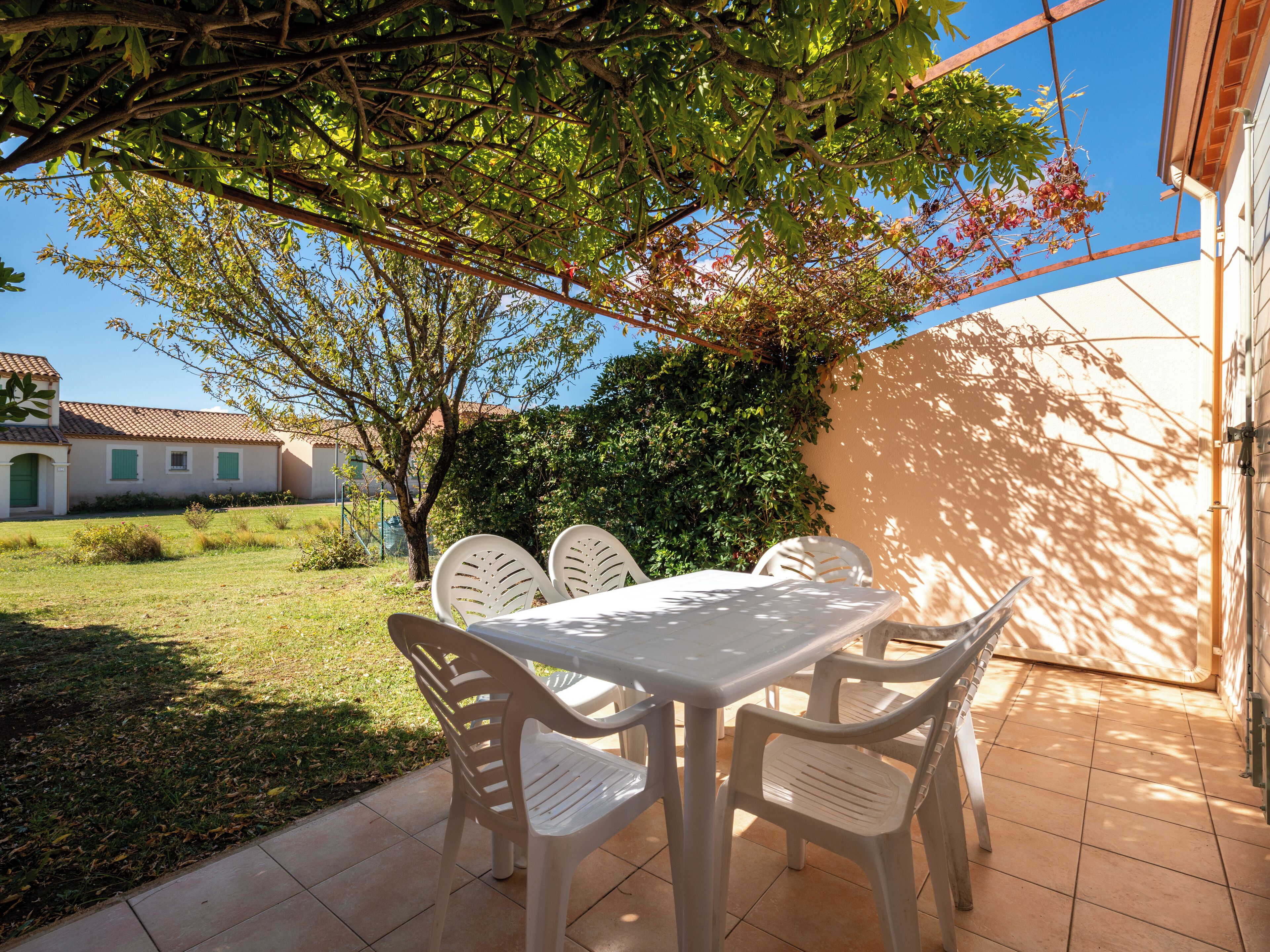 Eine Terrasse im Freien mit Tisch und Stühlen, umgeben von Pflanzen und einem Gebäude.