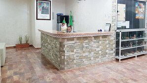 A reception area with a stone counter, a framed portrait, a flag, and a display cabinet with pottery. - Hotel Takialt (Adrar)