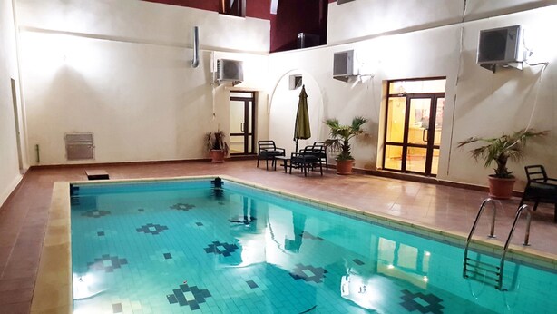 An indoor swimming pool with a tiled floor, a ladder, and potted plants. - Hotel Takialt (Adrar)