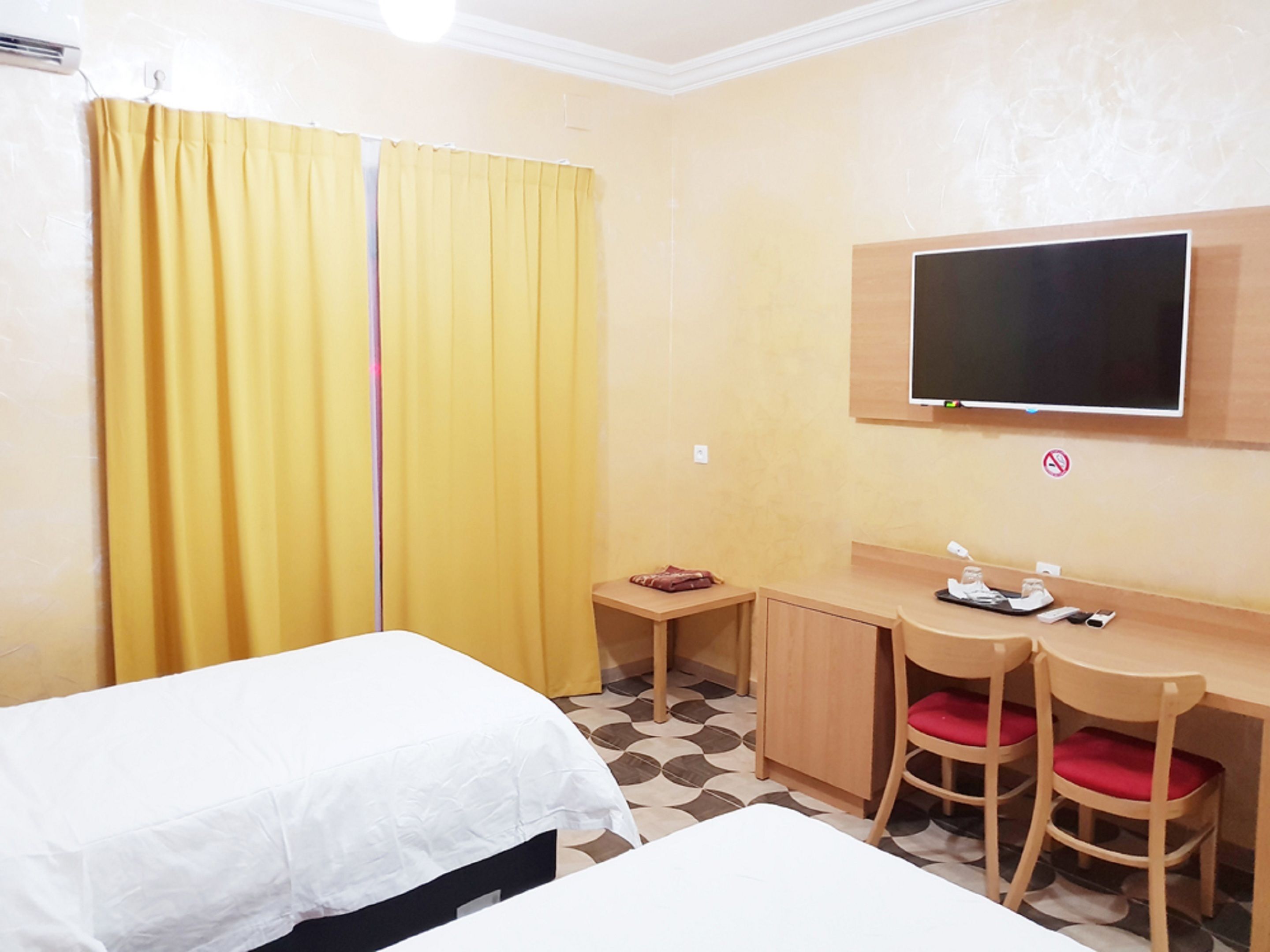 Habitación de hotel con dos camas, un escritorio, dos sillas, un televisor y una mesita con objetos encima.