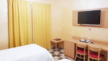 Habitación de hotel con dos camas, un escritorio, dos sillas, un televisor y una mesita con objetos encima.