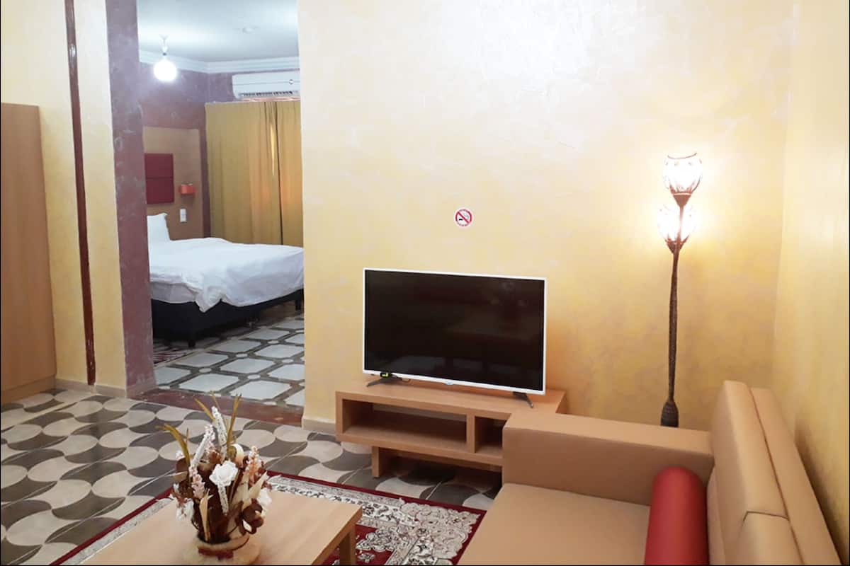 A hotel room with a TV, sofa, and a bed.