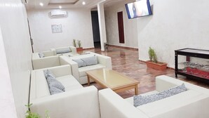 A modern lobby with white sofas, a wooden coffee table, and a flat-screen TV mounted on the wall. - Hotel Takialt (Adrar)