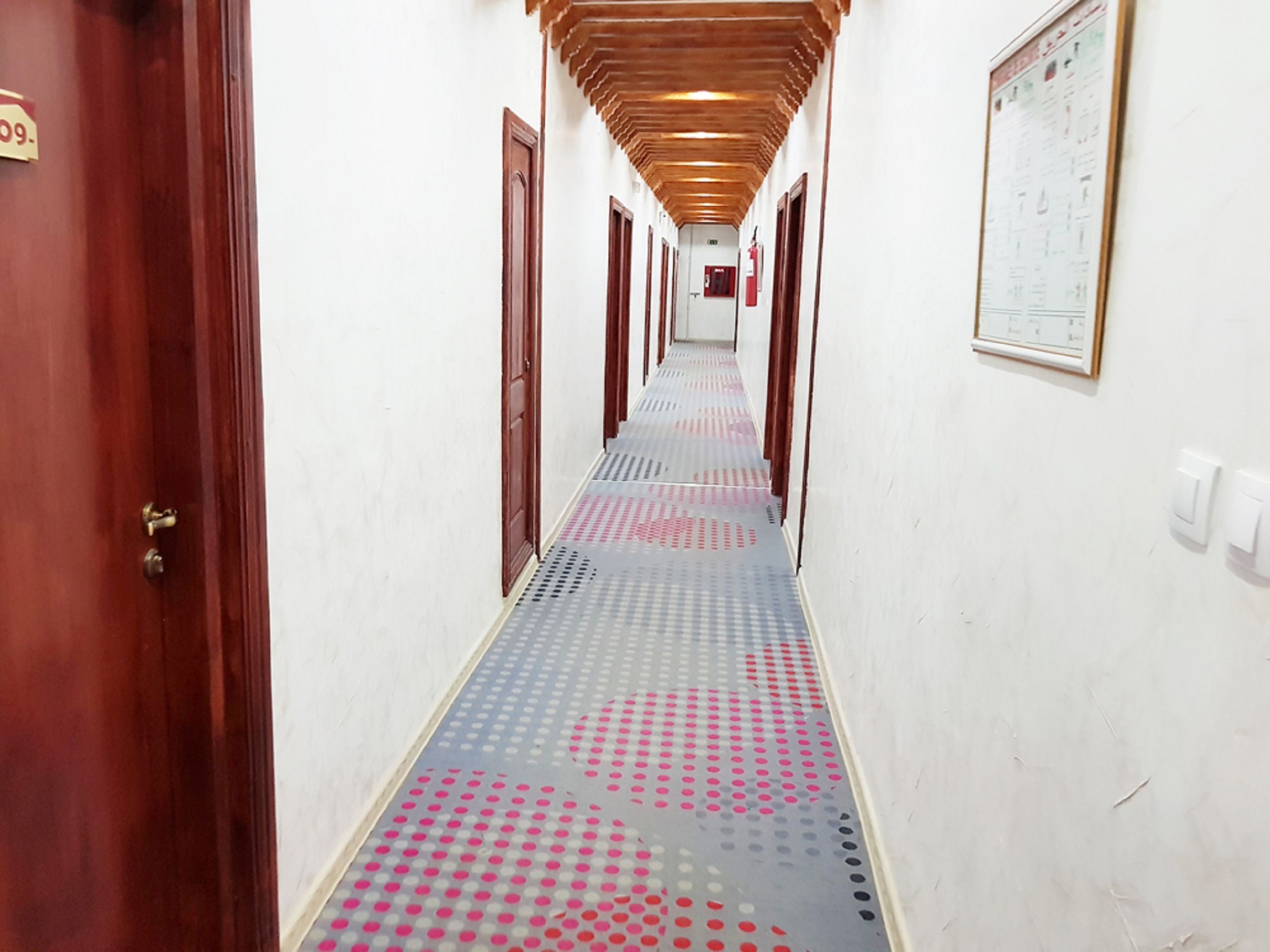 A hotel hallway with a patterned floor, wooden doors, and a fire safety poster on the wall.
