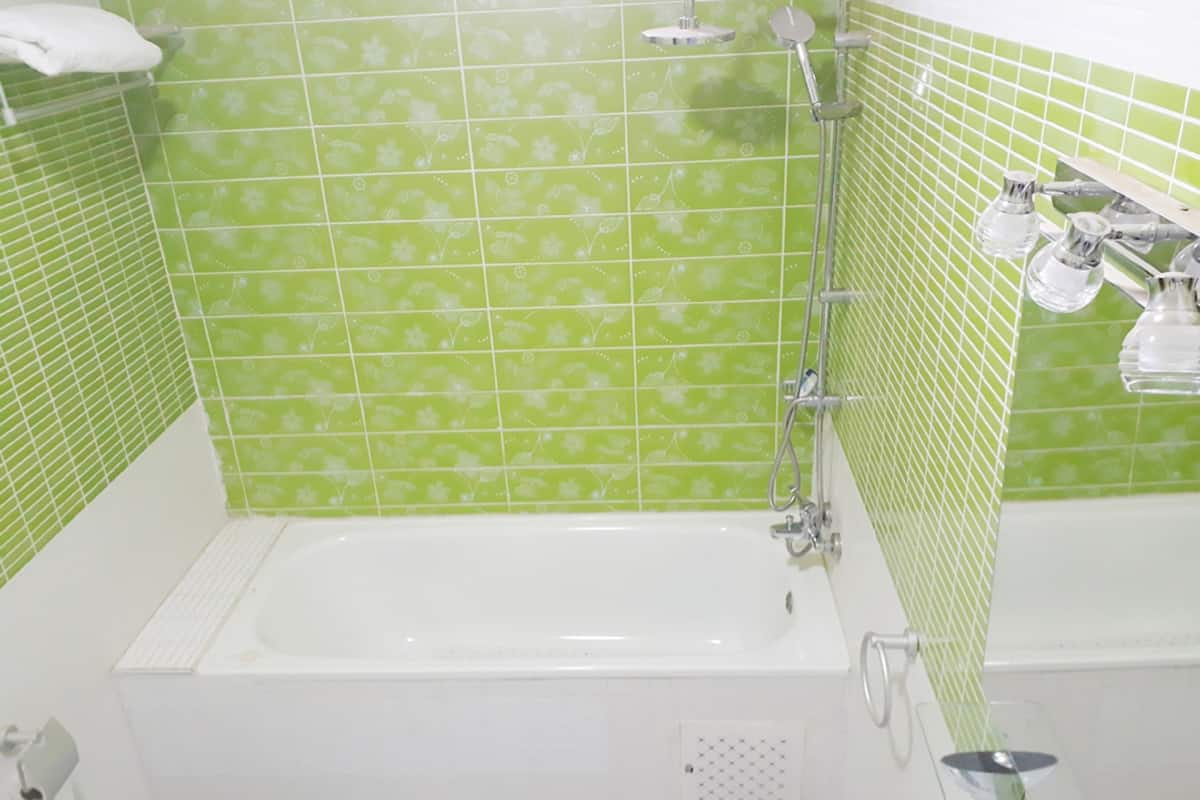 A bathroom with a white bathtub, green patterned tiles, and a shower area with chrome fixtures.