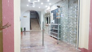 A reception area with a staircase leading to an upper floor, a reception desk, and a display case with items. - Hotel Takialt (Adrar)