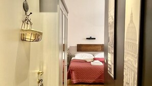 A narrow hallway leading to a bedroom with a bed, a wooden floor, and a wall-mounted shelf with a decorative item. - Roome B&B (Rome)