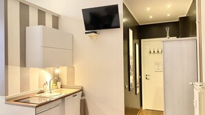 A compact kitchen with a built-in oven, a microwave, and a sink. There is a flat-screen TV mounted on the wall above the counter. - Roome B&B (Rome)