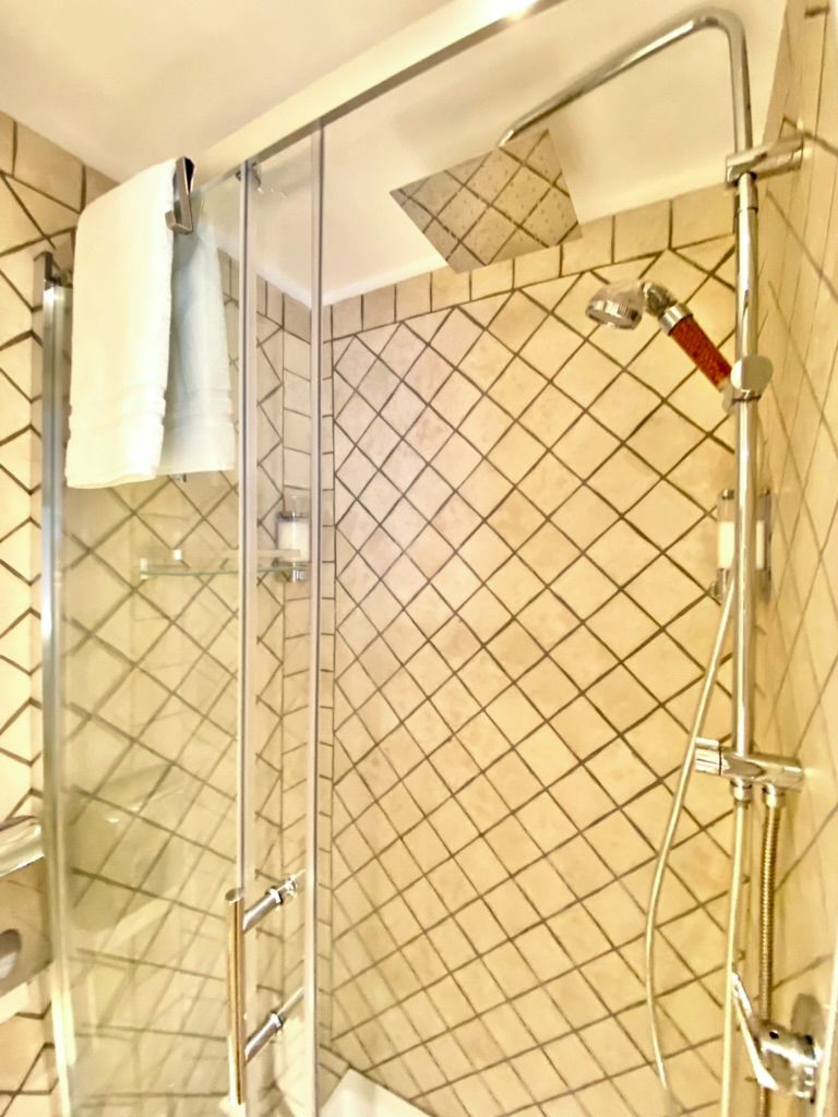 Et brusebad med glasvægge og vægfliser med diamantmønster.