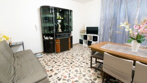 A living room with a sofa, a dining table with chairs, a glass cabinet, and a TV. - B&B Casa Anna Maria (Porto Sant'Elpidio)