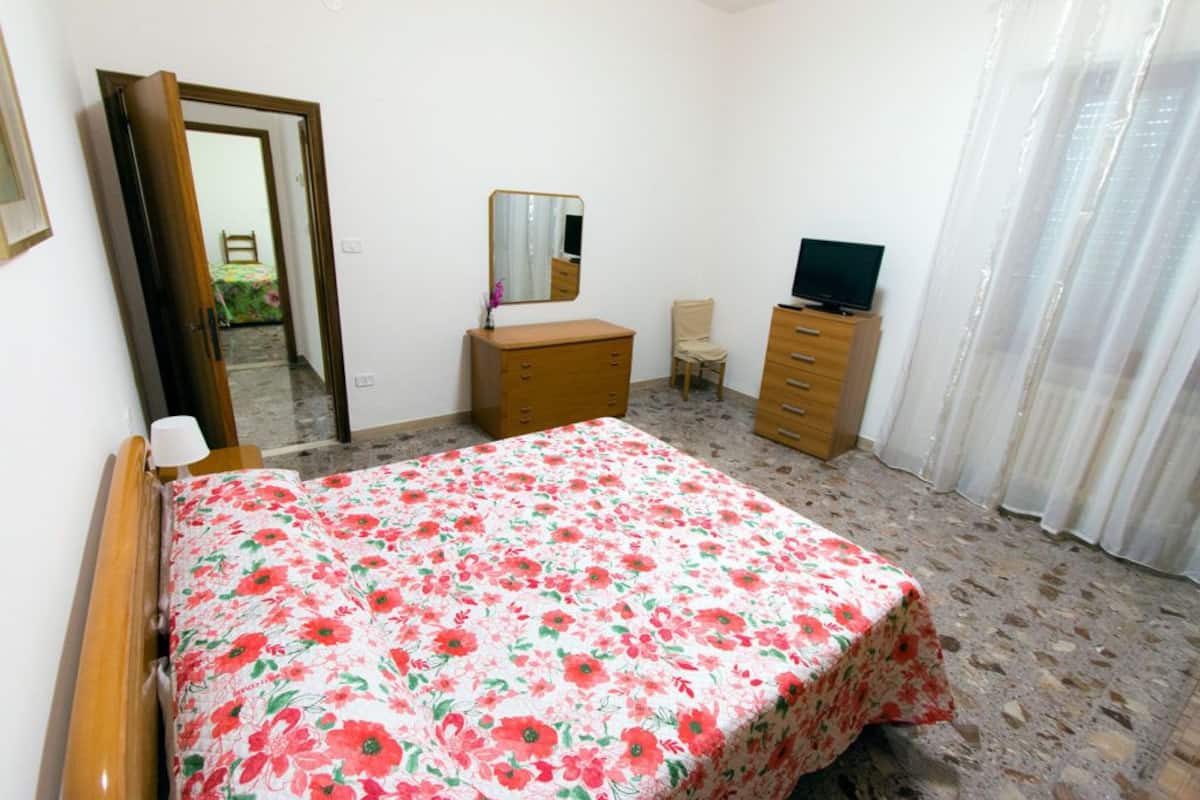 A bedroom with a bed, a dresser, a chair, a television, and a mirror.