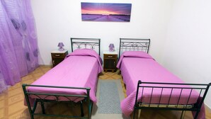 A room with two single beds, a nightstand with a lamp, a painting on the wall, and a purple curtain. - B&B Casa Anna Maria (Porto Sant'Elpidio)