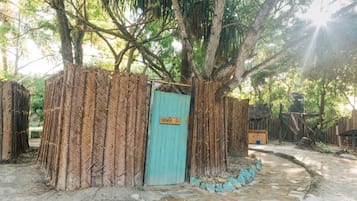 Una estructura de madera rústica con una puerta que indica “SHOWER 2”, rodeada de paredes de bambú trenzado.