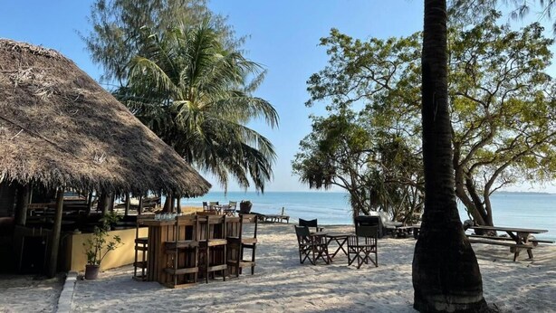 A beachside café with outdoor seating, a thatched-roof structure, and palm trees. - Mikadi Beach Camp (Dar es Salaam)