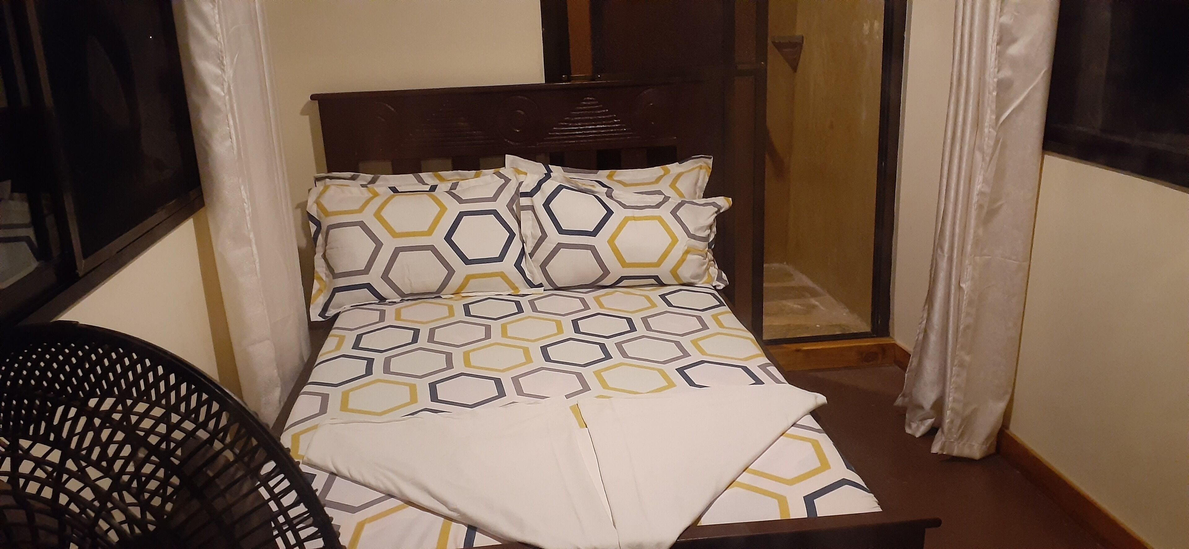 Uma cama pequena e bem arrumada, com roupa de cama estampada, cabeceira de madeira e uma janela com cortinas.