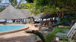 A pool area with a thatched roof structure, wooden benches, and potted plants. - Mikadi Beach Camp (Dar es Salaam)