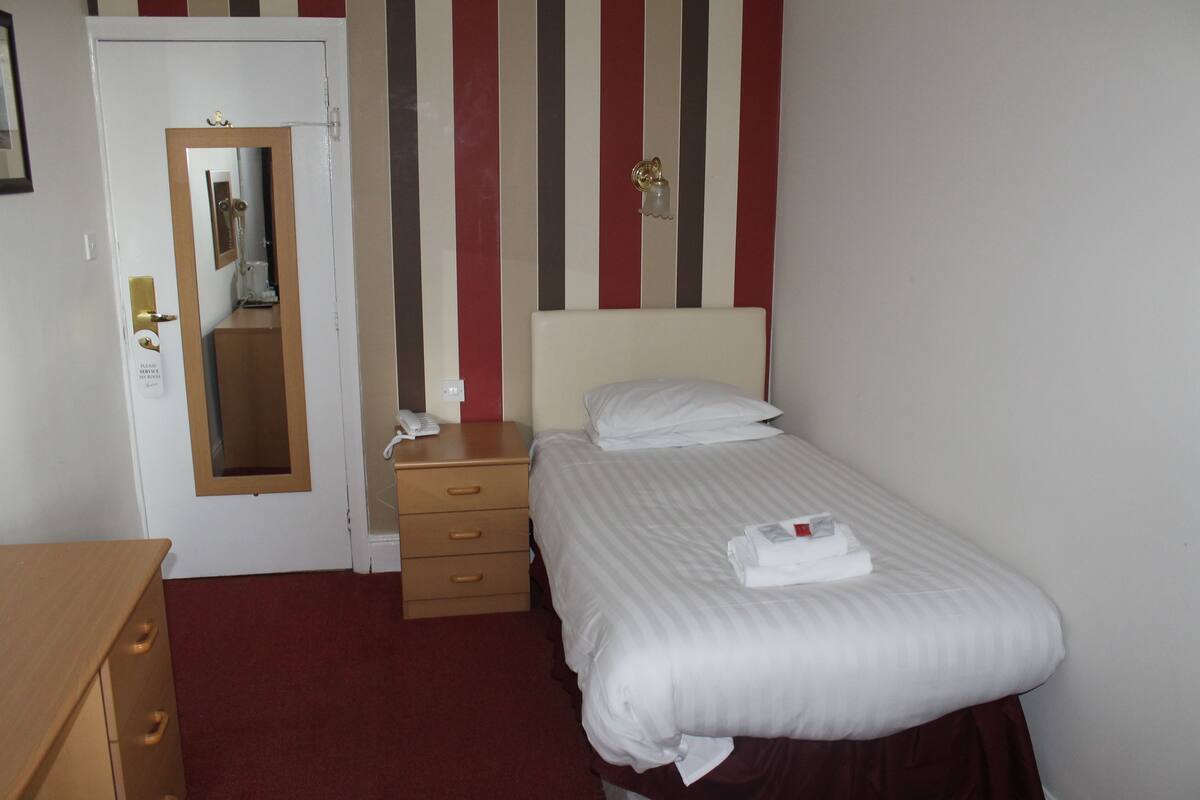 Een hotelkamer met een bed, een houten dressoir, een nachtkastje, een spiegel en een gestreepte wand.