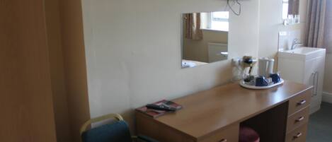 Ein Hotelzimmer mit Holztisch, Stuhl, Wandfernseher, Spiegel, Waschbecken und einem Vorhangfenster.