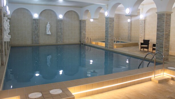 A large indoor swimming pool with a tiled floor and walls, surrounded by arched alcoves and stone pillars. - Chatsworth House Hotel (Llandudno)