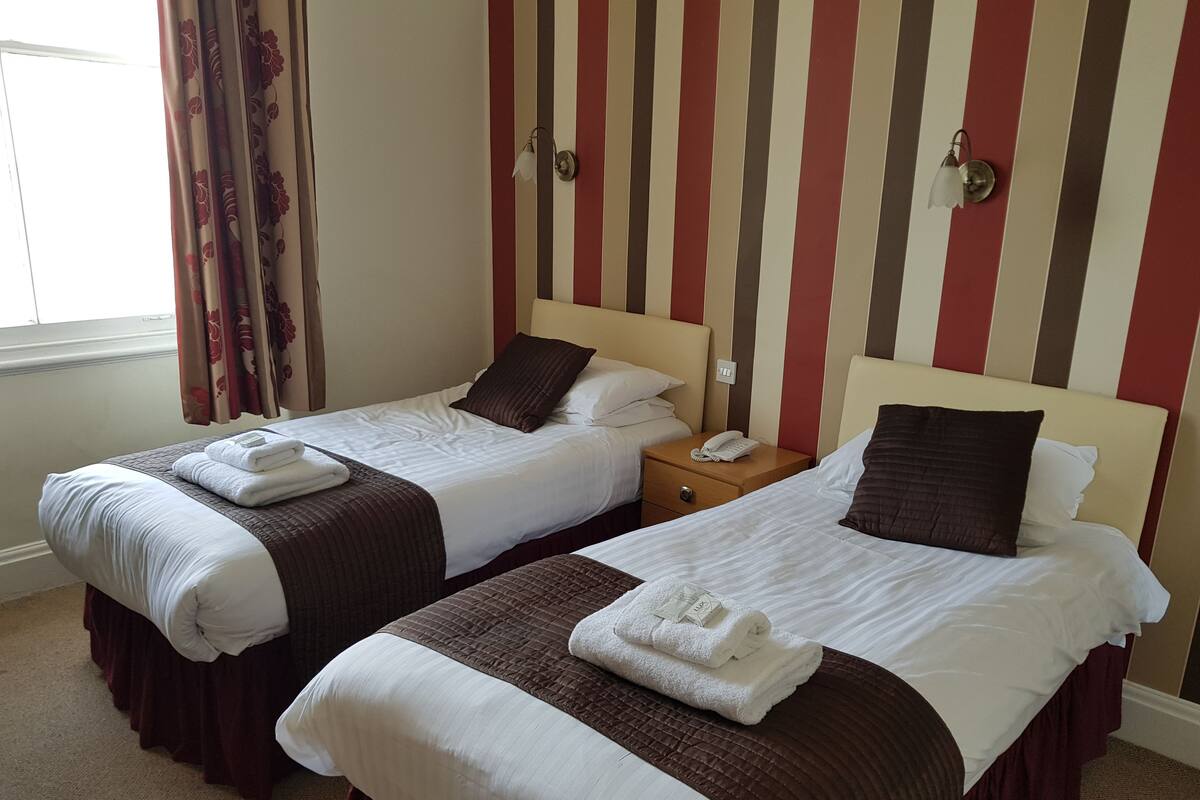 Een hotelkamer met twee bedden, elk met een bruin hoofdbord, wit beddengoed en een nachtkastje met een telefoon.