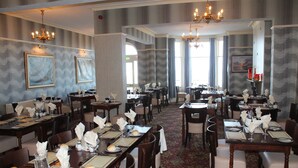 A formal dining room with multiple tables set for service, chandeliers, and framed artwork on the walls. - Chatsworth House Hotel (Llandudno)