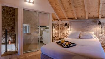 Une chambre avec un mur en pierre, un lit sur lequel est posé un plateau de petit-déjeuner, et un plafond en bois.