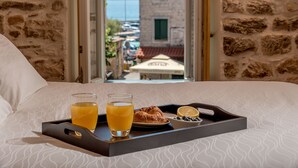 A hotel room with a bed, a tray with breakfast items, and a view of a building and water. - Boutique Properties Balturio - Stay Unique! (Kastela)
