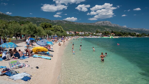 A beach with clear water, people swimming, and umbrellas. - Boutique Properties Balturio - Stay Unique! (Kastela)