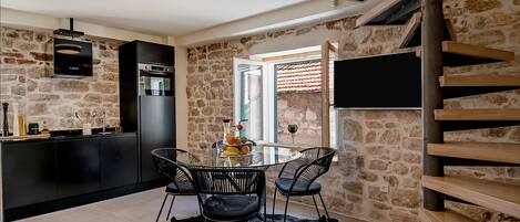 Une cuisine moderne avec un mur en pierre, un coin repas doté d’une table en verre et un escalier avec des marches en bois.