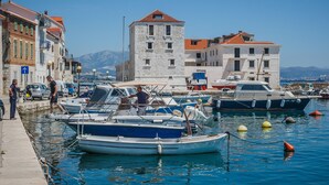 A marina with boats docked, a stone tower, and buildings with red-tiled roofs. - Boutique Properties Balturio - Stay Unique! (Kastela)