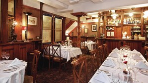 Un restaurant avec plusieurs tables dressées pour le service, des boiseries et un bar où sont exposées des bouteilles.