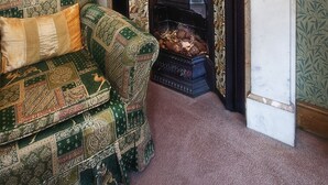 Une pièce de style traditionnel, dotée d’une cheminée, d’un papier peint à motifs et d’un tableau encadré au-dessus de la cheminée.