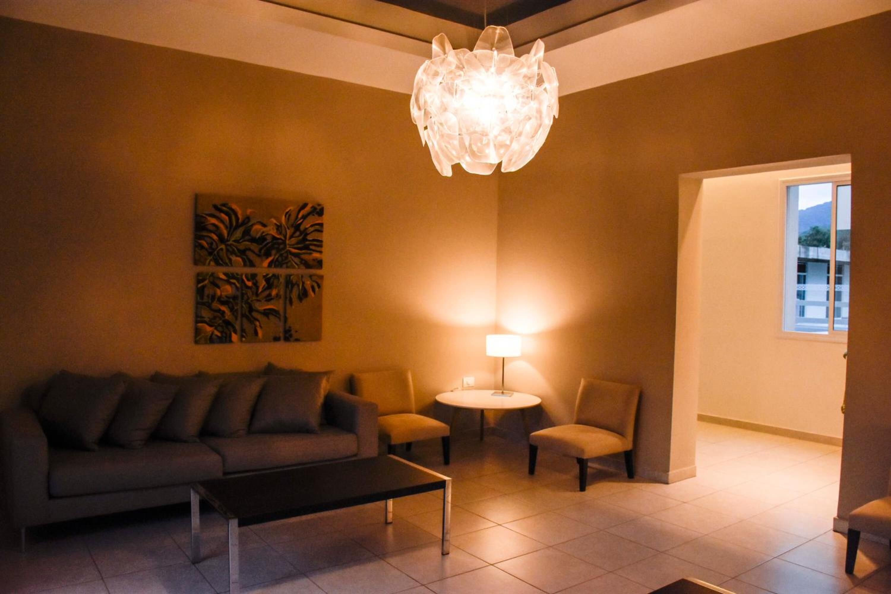 A living room with a sofa, armchairs, a coffee table, a lamp, and a wall art piece.