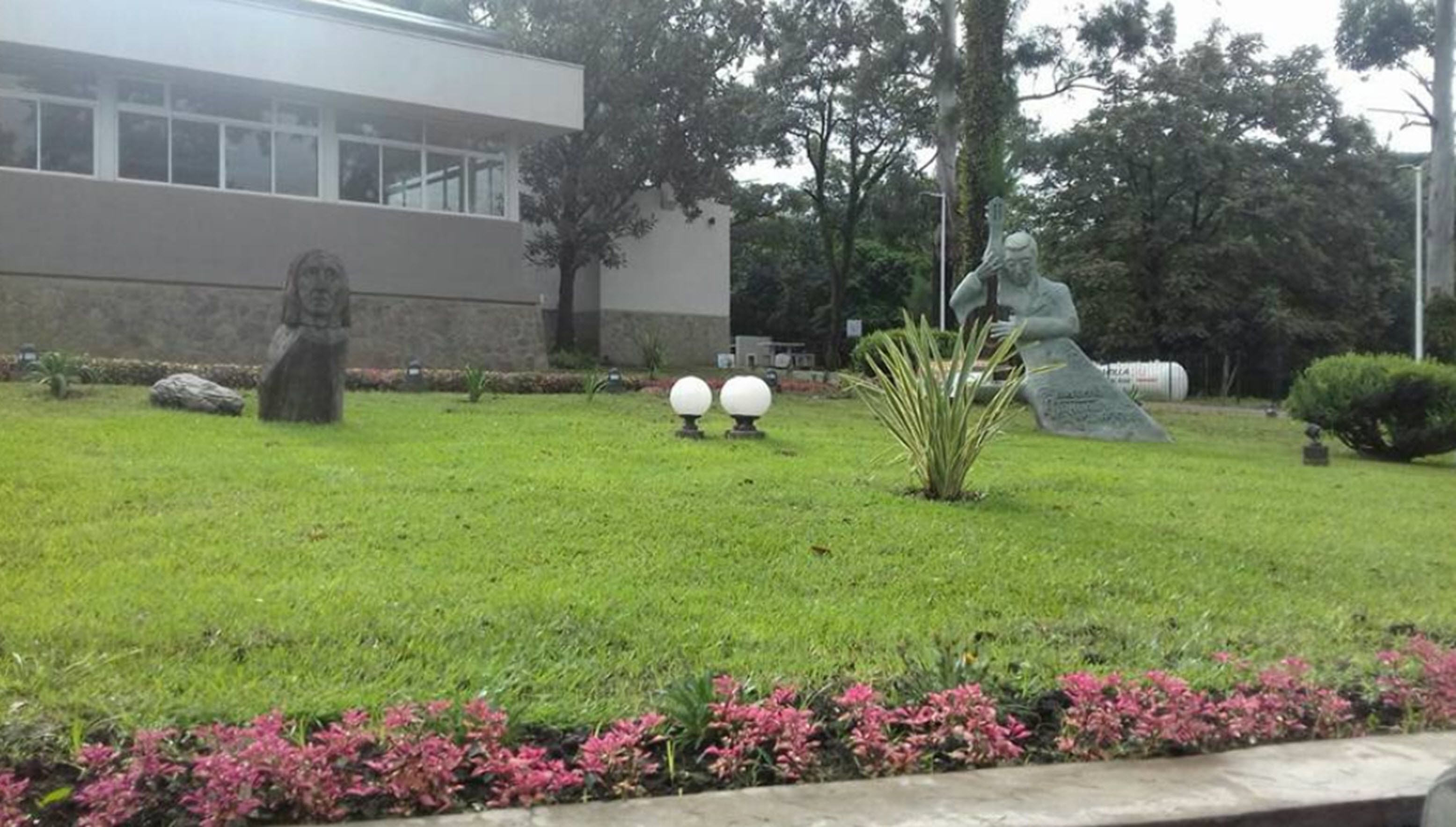 Uma área gramada com uma estátua, um edifício e um monumento de pedra.