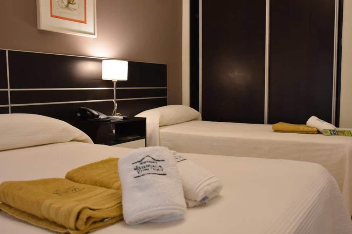 Habitación de hotel con dos camas, una mesita de noche con lámpara y toallas sobre la cama.